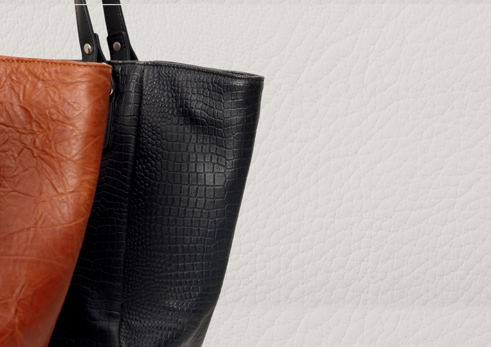 Tan crinkled leather tote beside a black croc-embossed tote on white grained leather